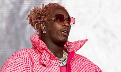 A closeup of Young Thug performing at Lollapalooza in 2021. He is wearing a pink coat and pink tinted glasses.