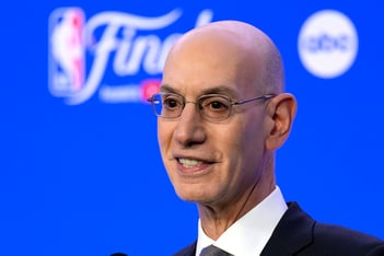NBA Commissioner Adam Silver talks in front of a bright blue background.