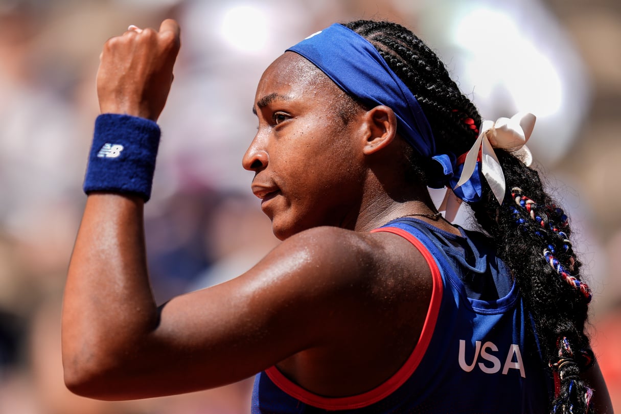 Coco Gauff, U.S. tennis Olympian, has a hand raised in the air while looking to the left.