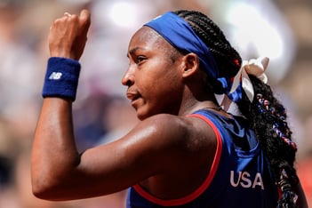 Coco Gauff, U.S. tennis Olympian, has a hand raised in the air while looking to the left.