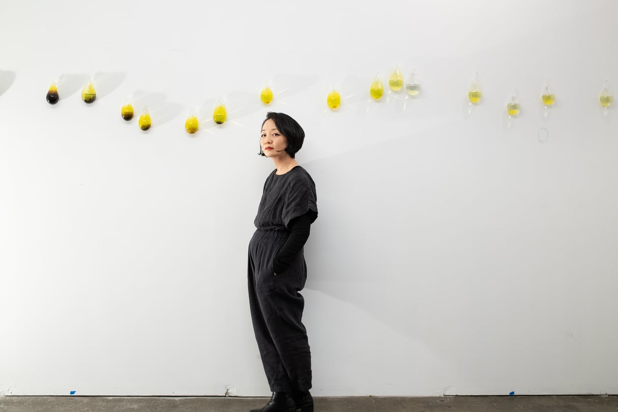 Gyun Hur stands beside her hand-blown glass vessels of local river water in her studio.