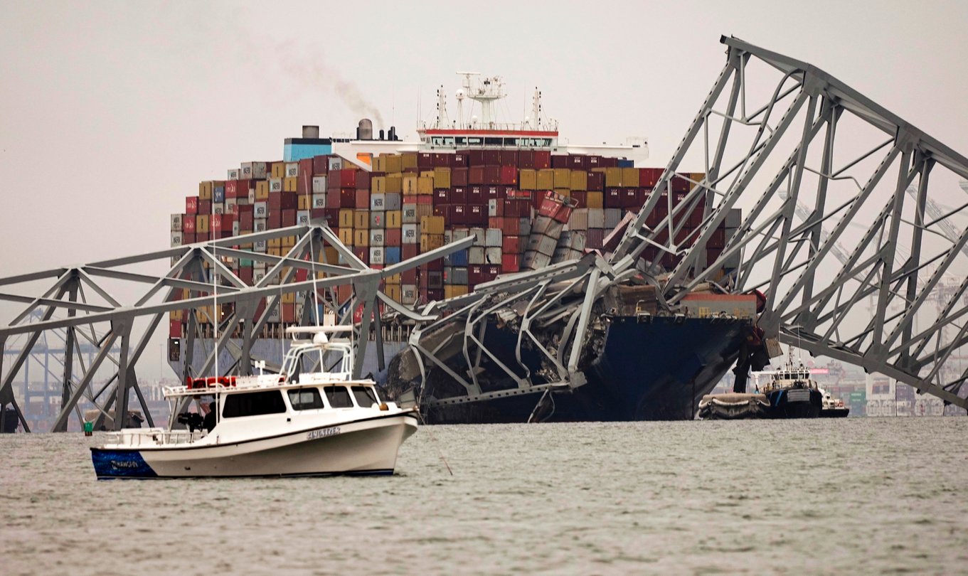 A small boat is anchored in front of a cargo ship that is stuck under the part of the structure of the Francis Scott Key Bridge after the ship hit the bridge Wednesday, March 27, 2024, in Baltimore, Md.