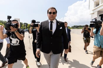 Former U.S. Rep. George Santos arrives at court in Central Islip, N.Y. He walks forward, wearing sunglasses, while cameras point at him.