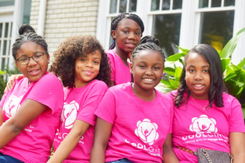 Several young girls wearing bright pink Cool Girls T-shirts pose for a photo.