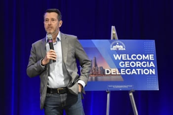 David Plouffe stands with a microphone at the Democratic National Convention in front of a sign that says Welcome Georgia Delegation.