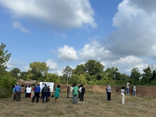 People mill around the Chattahoochee Brick Company site in front of a short, old brick wall. There's a white banner on the left about the Bipartisan Infrastructure Law.