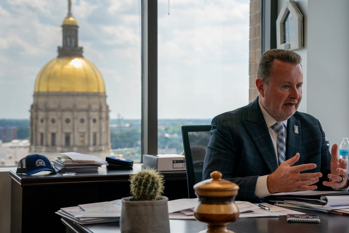 Kevin Tanner talks at a desk in front of a large window with the Gold Dome in the background