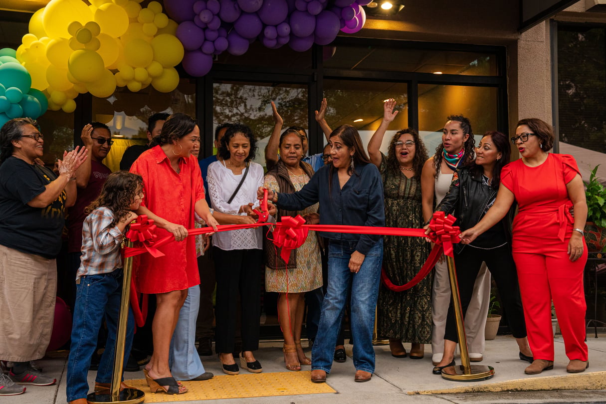 A group of people stand behind a large red ribbon as someone cuts it.