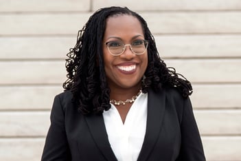 Supreme Court Justice Ketanji Brown Jackson is smiling in front of a white wall.