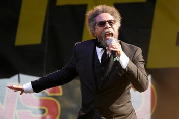 Cornel West speaks into a microphone, holding one hand out