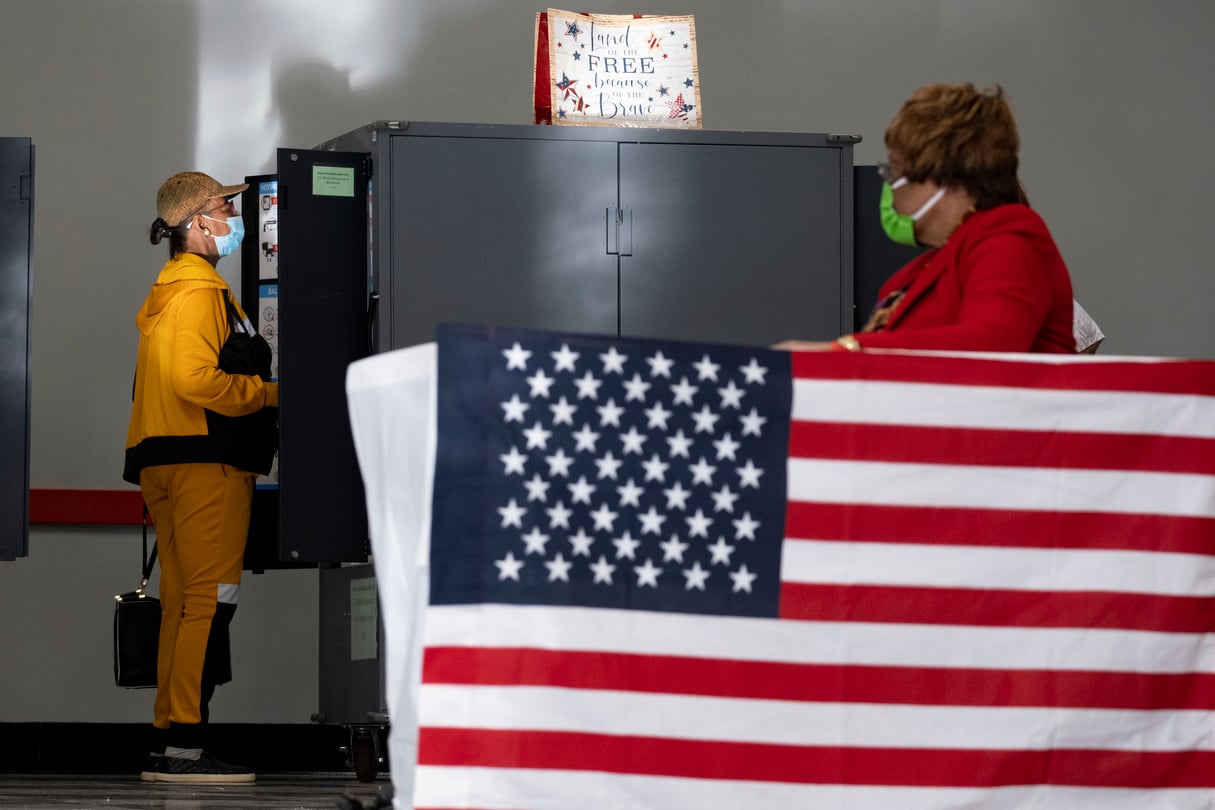 A voter marks her ballot during the first day of early voting in Atlanta, Oct. 17, 2022. A large American flag is next to the ballot boxes.
