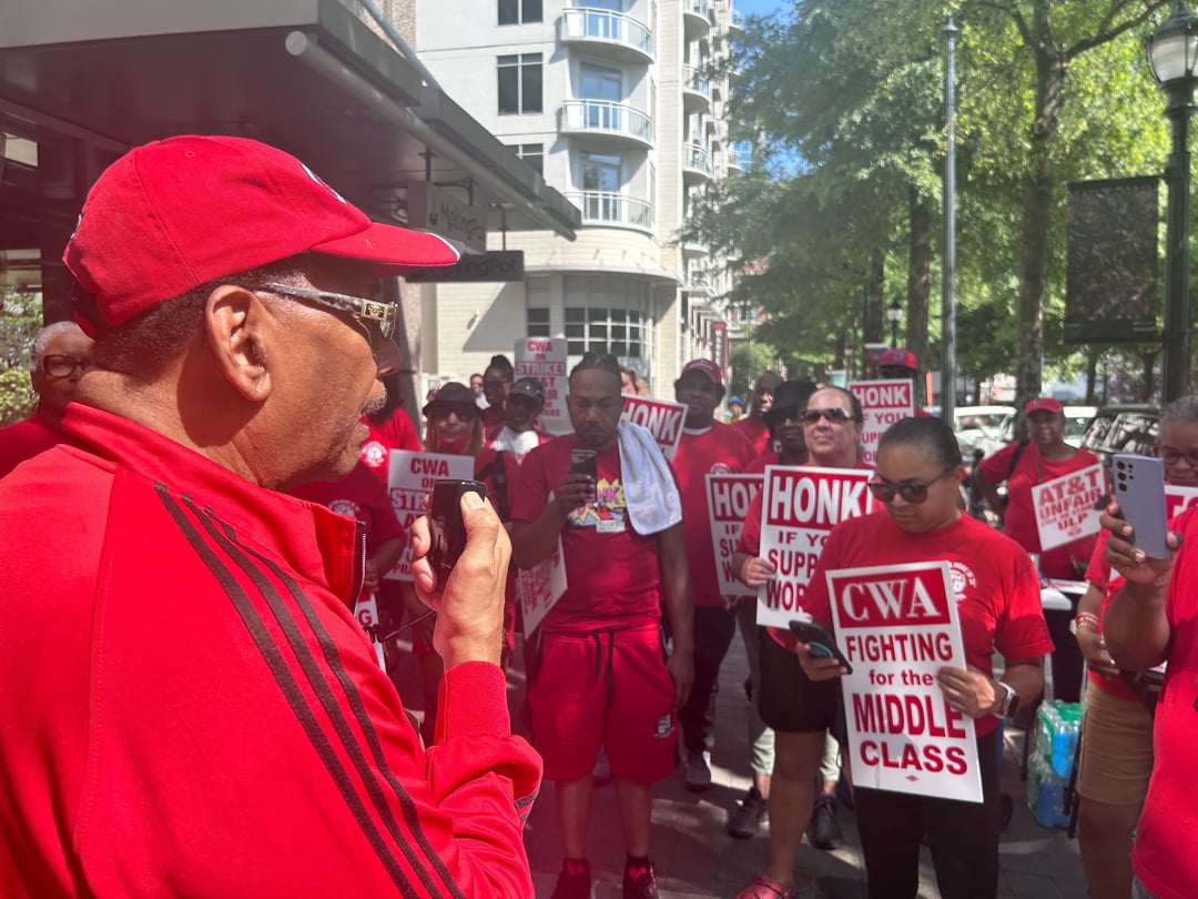 CWA President Claude Cummings Jr. speaks as striking workers listen. All wear red CWA shirts.