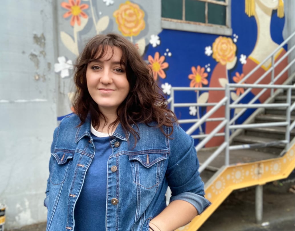 Nicole Merizalde poses in front of a blue and yellow mural behind a staircase.
