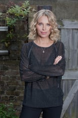 Nikki Bedi poses for a photograph against a wooden fence.