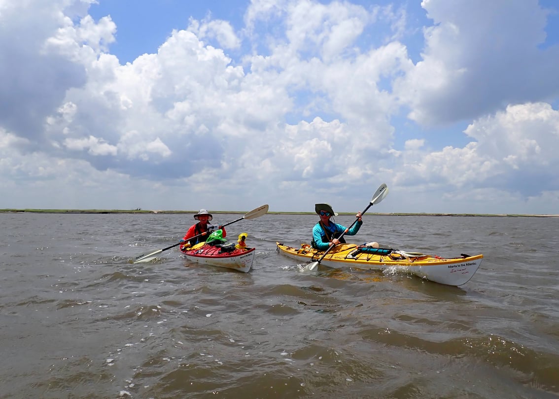 Two people in kayaks under a blue sky.