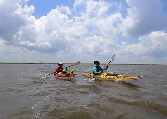 Two people in kayaks under a blue sky.