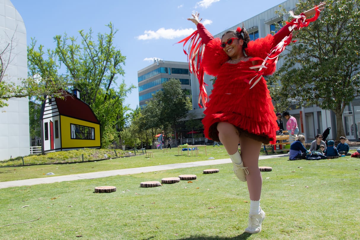 A person is running around in a backyard, wearing a shirt with red tassels and a red dress.
