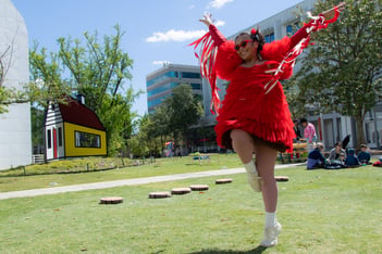 A person is running around in a backyard, wearing a shirt with red tassels and a red dress.
