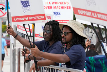 Dockworkers on strike hold up signs.