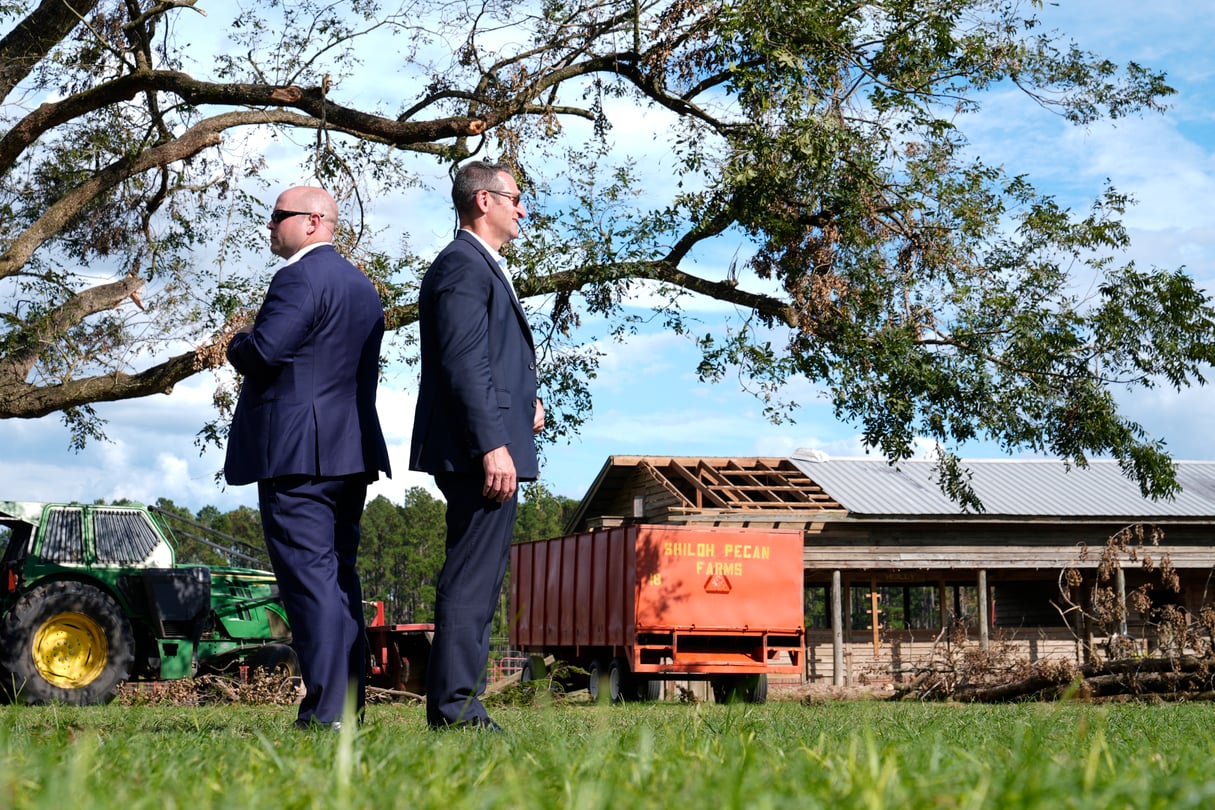 Two members of the Secret Service stand back-to-back at Shiloh Pecan Farm in Georgia as Biden speaks out of the frame.