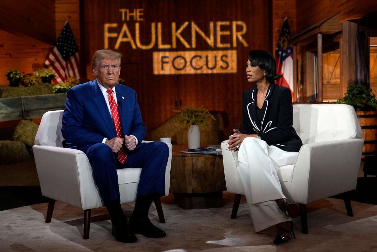 Donald Trump sits on a white armchair to the left, and journalist Harris Faulkner sits in a white armchair to the right. The Faulkner Focus logo is projected onto the wood background.
