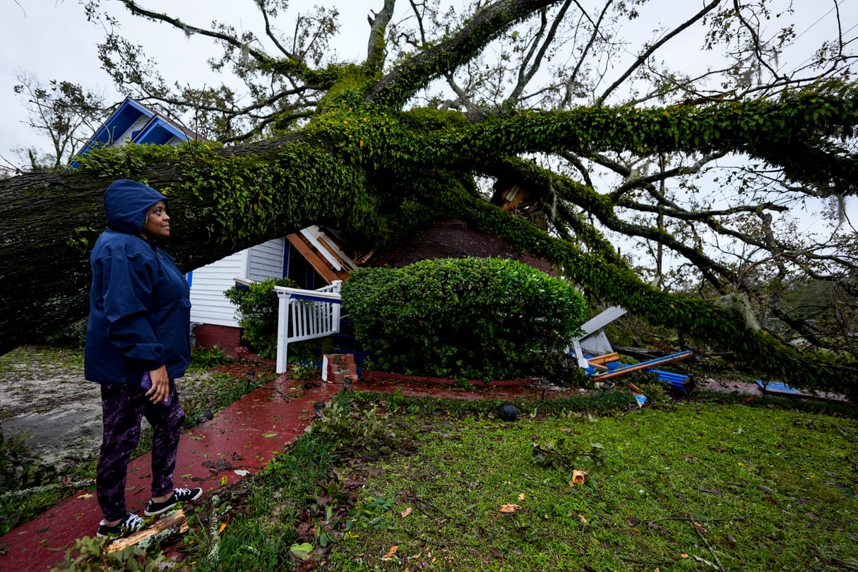 A woman stands to the left and looks at a giant oak tree that landed on her 100-year-old home in Valdosta, Georgia.