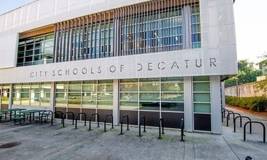A rectangular building with large windows and a white, modern exterior. There are bars over the windows on the top floor.