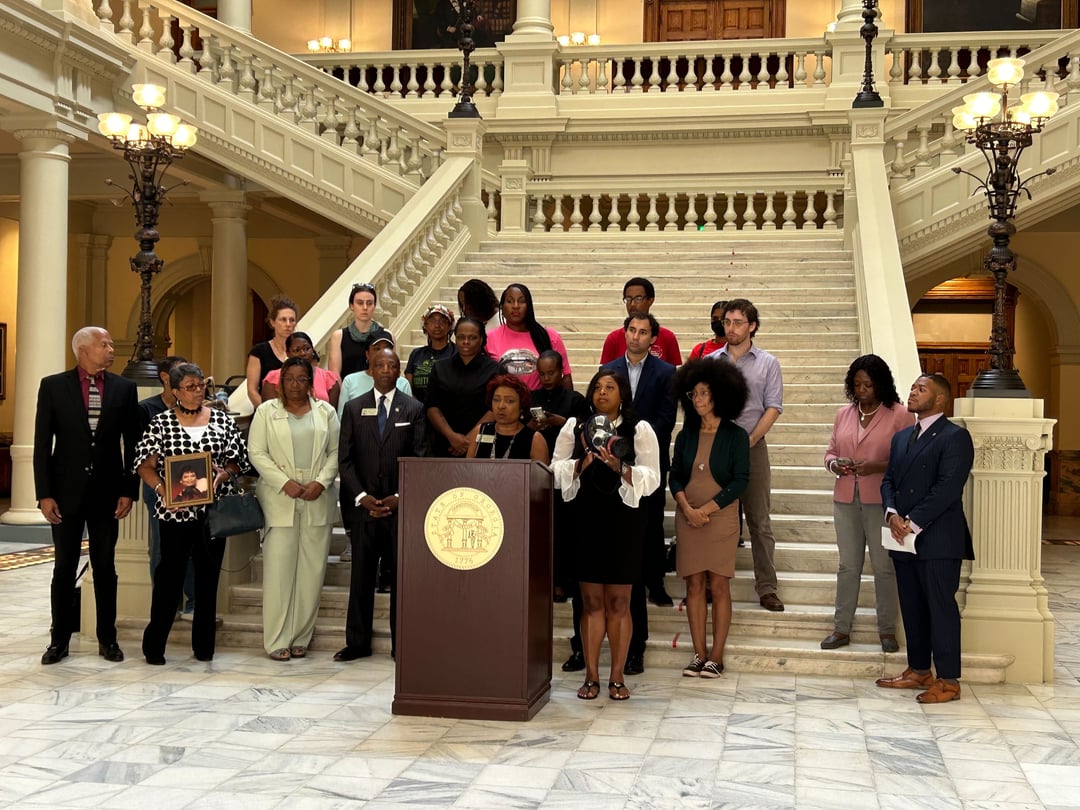A group of people stand at the bottom of a staircase in the Georgia State Capitol for a press conference.