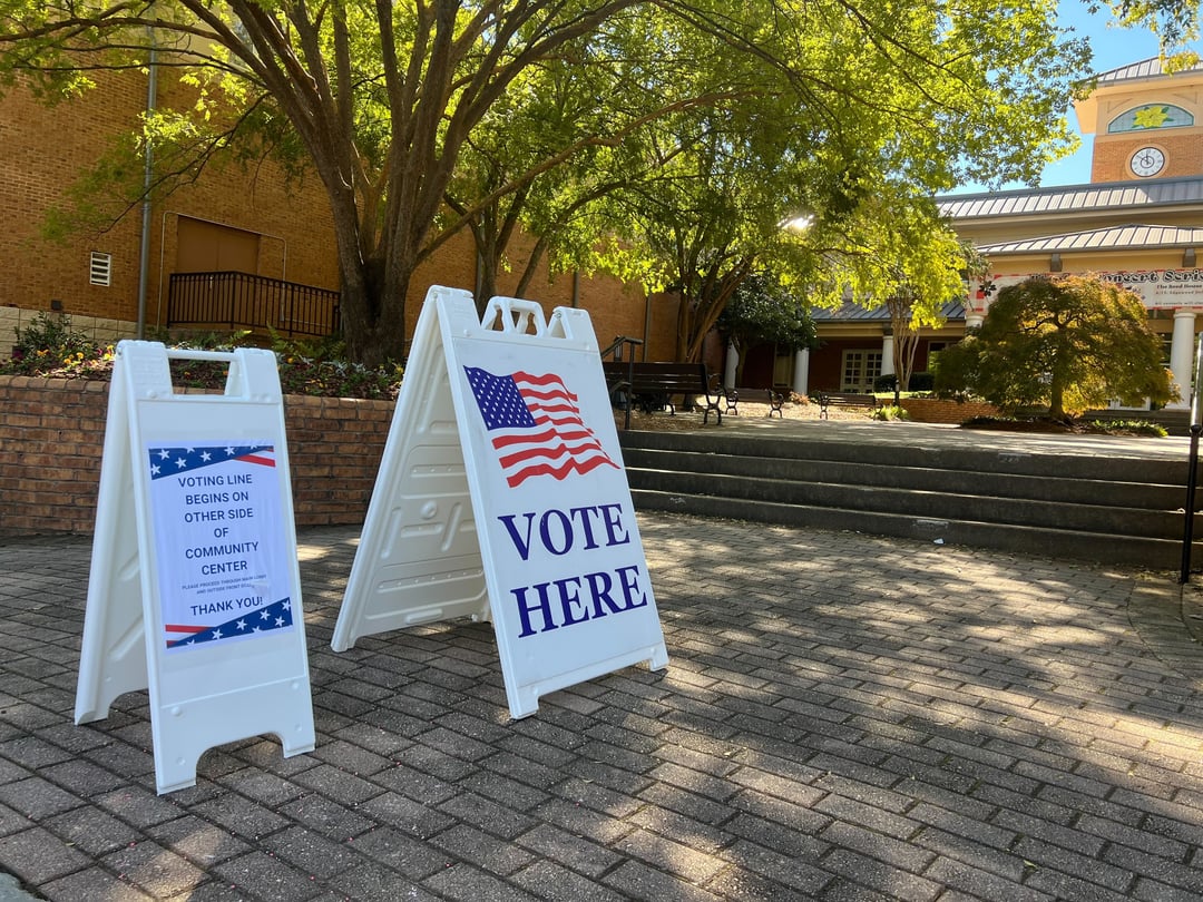 A vote sign in front of a polling location underneath a tree.
