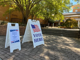 A vote sign in front of a polling location underneath a tree.