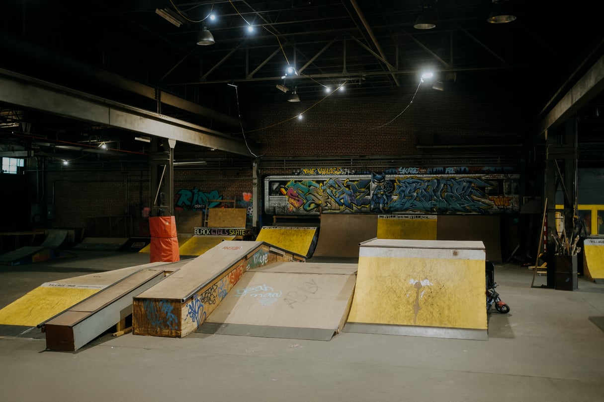 An overhead view of an indoor skatepark, with yellow and wood-colored ramps and graffiti artwork on the walls.