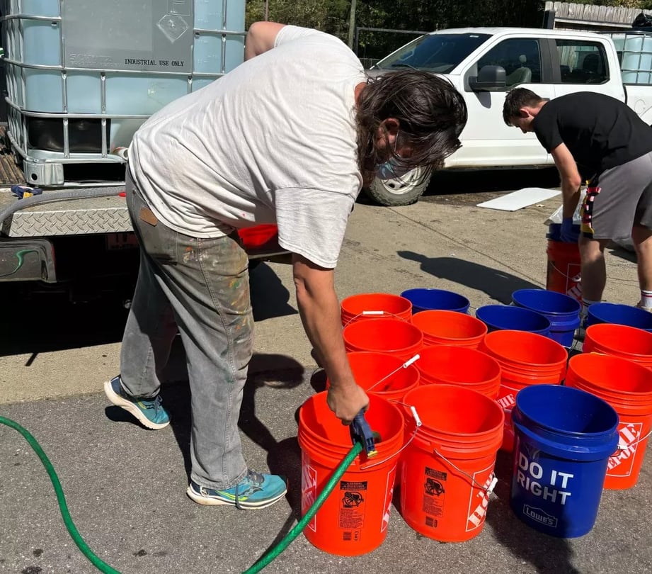 Jerry Cahill fills several orange buckets with a hose.