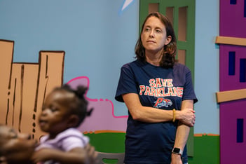 A parent looks off into the distance in front of a colorful wall. A child is in the foreground.