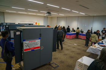 Election machines are shown in a room of voters casting their votes