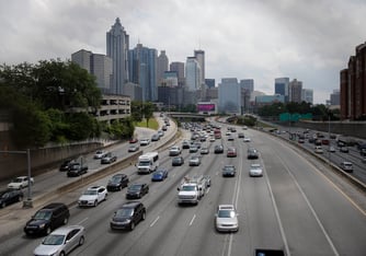 Cars on the highway are shown in the foreground while the buildings of downtown atlanta are in the background on an overcast day
