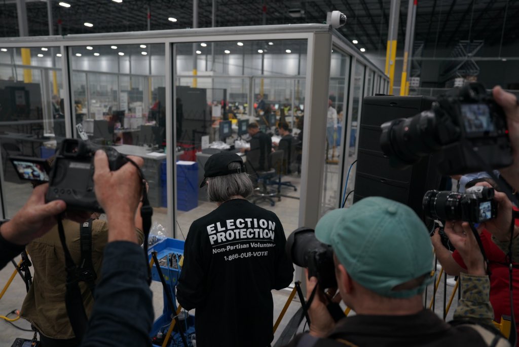 Fulton County election workers upload voting results data from the memory card of the machines used during early voting while observers watch from outside the glass.