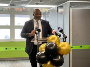 Atlanta Public Schools Superintendent Bryan Johnson speaks at a clear podium with black and yellow balloons, holding a microphone, standing in front of a green ribbon.