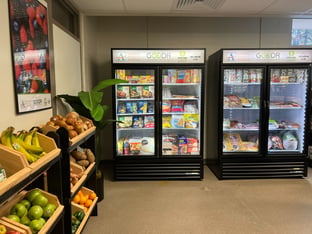 A grocery store with two freezers and a rack of produce.