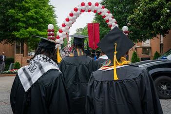 A group of graduates donning black robes walk toward a red and white balloon arch