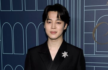 BTS member Jimin wearing a black suit and a broach.