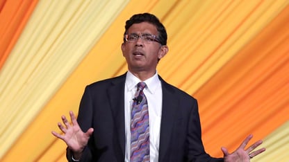 Dinesh D'Souza speaks in front of an orange background.