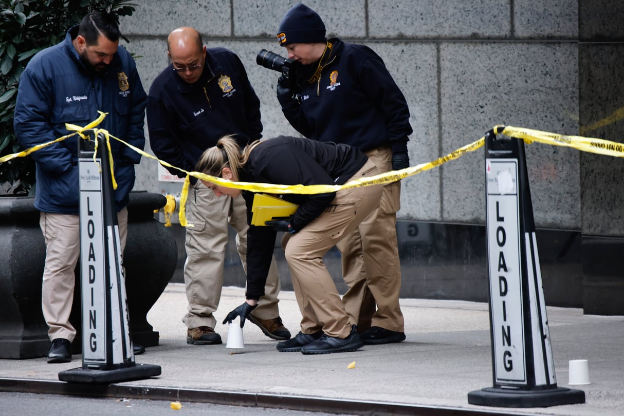 Multiple law enforcement menbers kneeling near the scene of a crime in Manhattan.