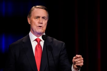 David Perdue wearing a red tie speaking at a podium.