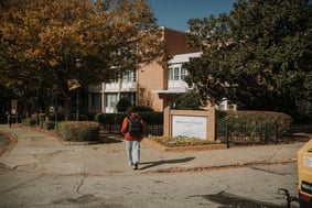 A student walks toward a building on the Morehouse College campus, next to a sign with the college's name on it.