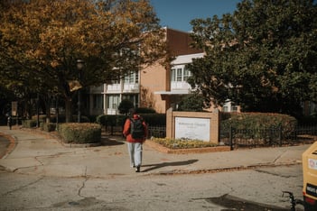 A student walks toward a building on the Morehouse College campus, next to a sign with the college's name on it.