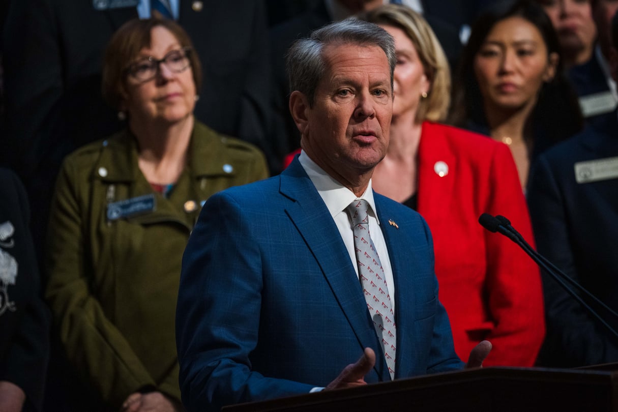 Kemp stands in front of a group of legislators at the Georgia State Capitol, speaking at a podium.