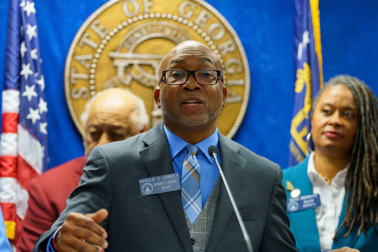 Georgia Senate Minority Leader Harold Jones at a presser in front of a blue background, a gold seal and several flags. He stands next to other Democrats.