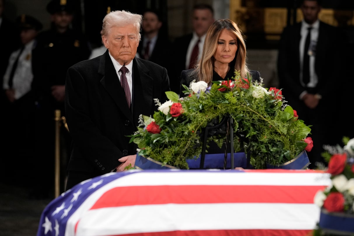 Donald and Melania Trump stand in front of the flag-draped casket of former President Jimmy Carter.