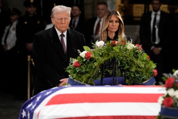 Donald and Melania Trump stand in front of the flag-draped casket of former President Jimmy Carter.