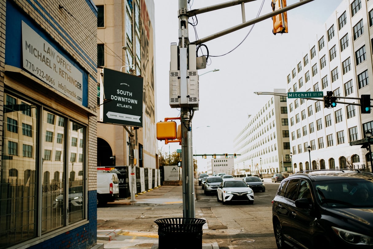 A street sign saying South Downtown in front of a storefront, facing a street light and cars.